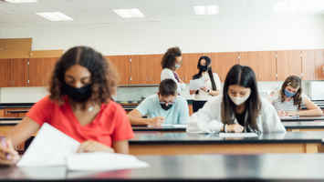 Diverse students working in the classroom during the pandemic, practicing safe learning techniques